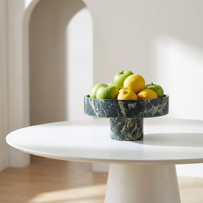 Green marble pedestal fruit bowl filled with apples and lemons on a white round pedestal table