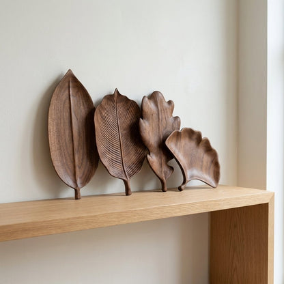 Four walnut leaf-shaped trays standing on edge against a wall on a light oak console table