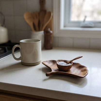 Ginkgo-shaped walnut tray with a small bowl of salt and a wooden spoon on a kitchen counter