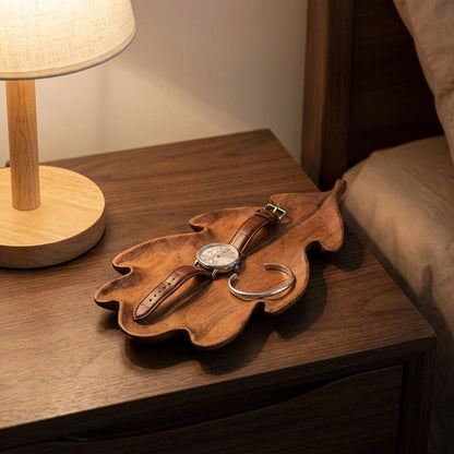Lobed walnut leaf tray holding a watch and silver cuff bracelet on a nightstand beside a lamp