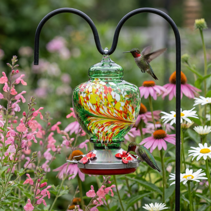 Handblown glass hummingbird feeder hanging in garden beside flowers