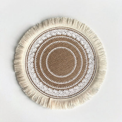 Round handwoven jute placemat with cream cotton fringe and white lace rings on a light grey background