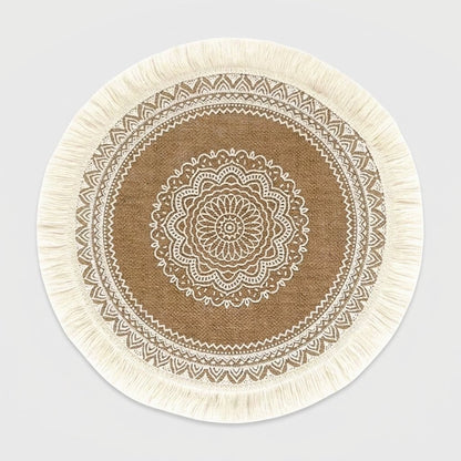 Round handwoven jute placemat with cream cotton fringe and a white mandala pattern on a light grey background