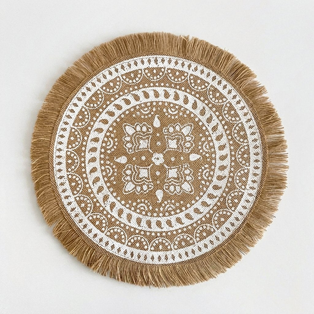 Round handwoven jute placemat with a white paisley pattern and jute fringe edge on a light grey background