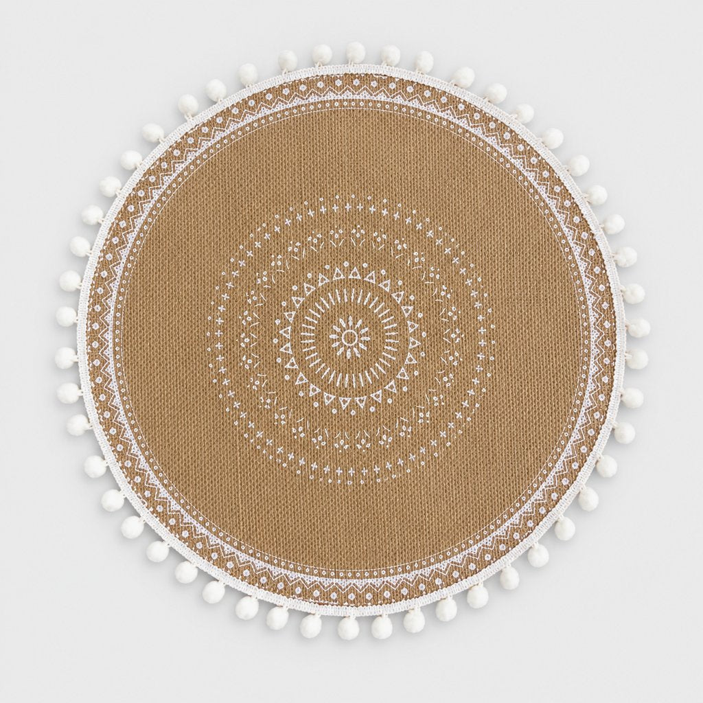 Round handwoven jute placemat with a white dotted mandala pattern, white pompom trim and a white band edge on a light grey background