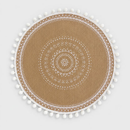 Round handwoven jute placemat with a white dotted mandala pattern, white pompom trim and a white band edge on a light grey background