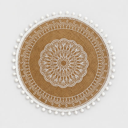 Round handwoven jute placemat with a white lace mandala pattern and white pompom trim on a light grey background