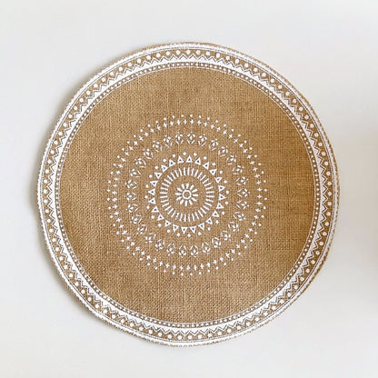 Round handwoven jute placemat with a white dotted mandala pattern and white trim edge, no fringe, on a light grey background