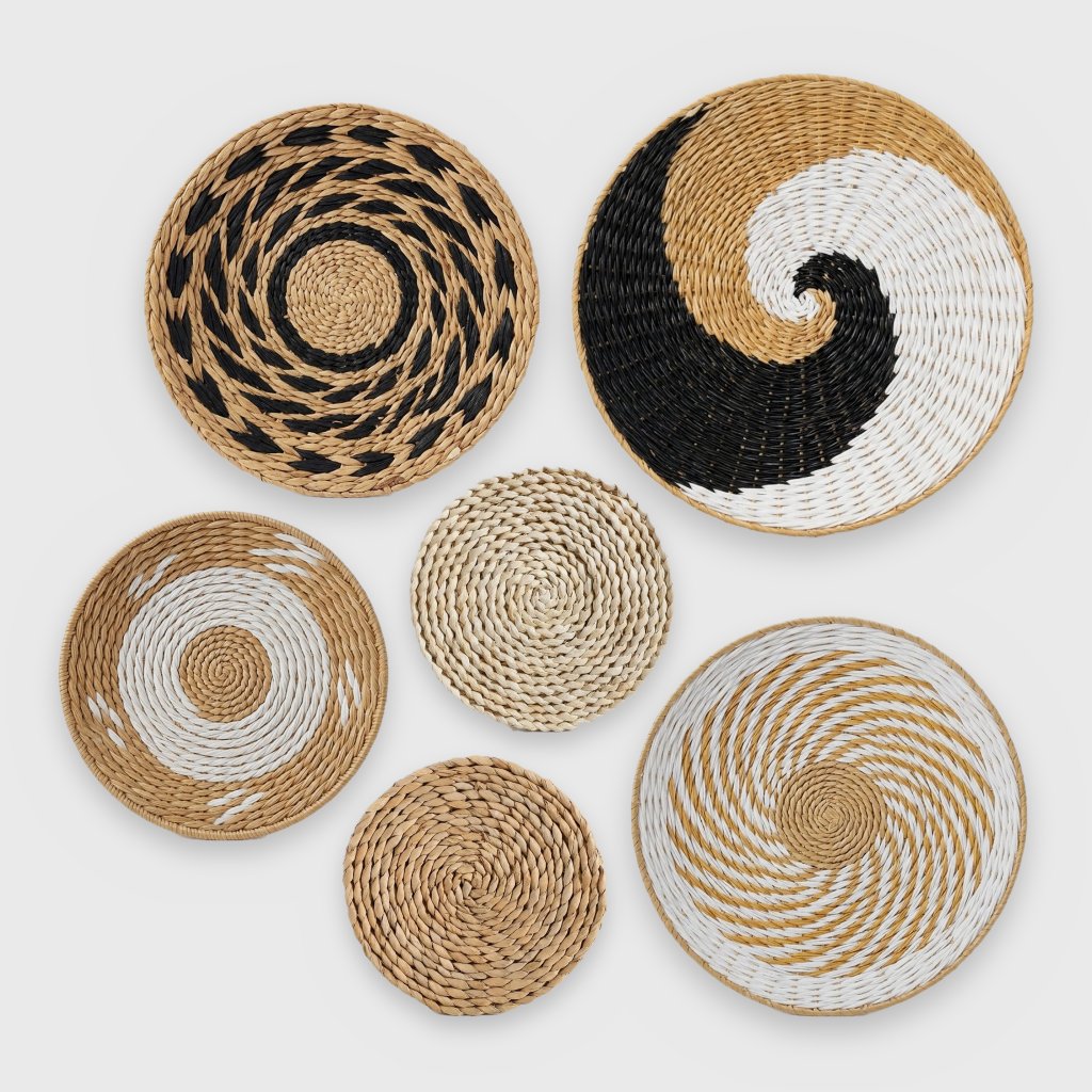 Six round woven wall baskets of different sizes and weaves in tan, black and white arranged on a plain light gray background