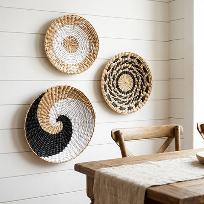 Three round woven wall baskets in tan, white and black patterns on a white shiplap wall above a rustic wood dining table with a linen runner