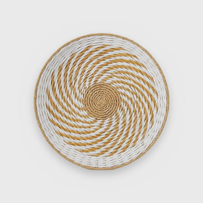 Single round woven basket with a tan center and white and golden-tan pinwheel spirals with a thin tan rim, on a plain light gray background
