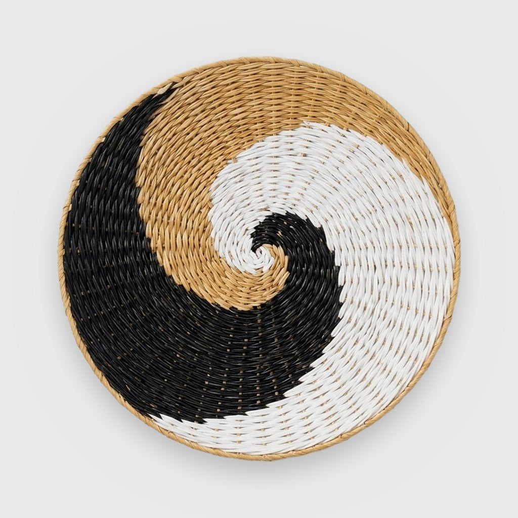 Single round woven basket with a black, white and tan wave swirl and a thin tan rim on a plain light gray background