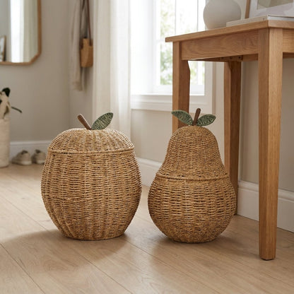 Apple-shaped and pear-shaped woven rattan lidded baskets with brown stems and green leaves side by side on a wood floor in an entryway
