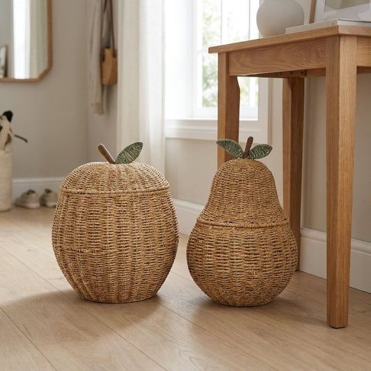 Apple-shaped and pear-shaped woven rattan lidded baskets with brown stems and green leaves side by side on a wood floor in an entryway