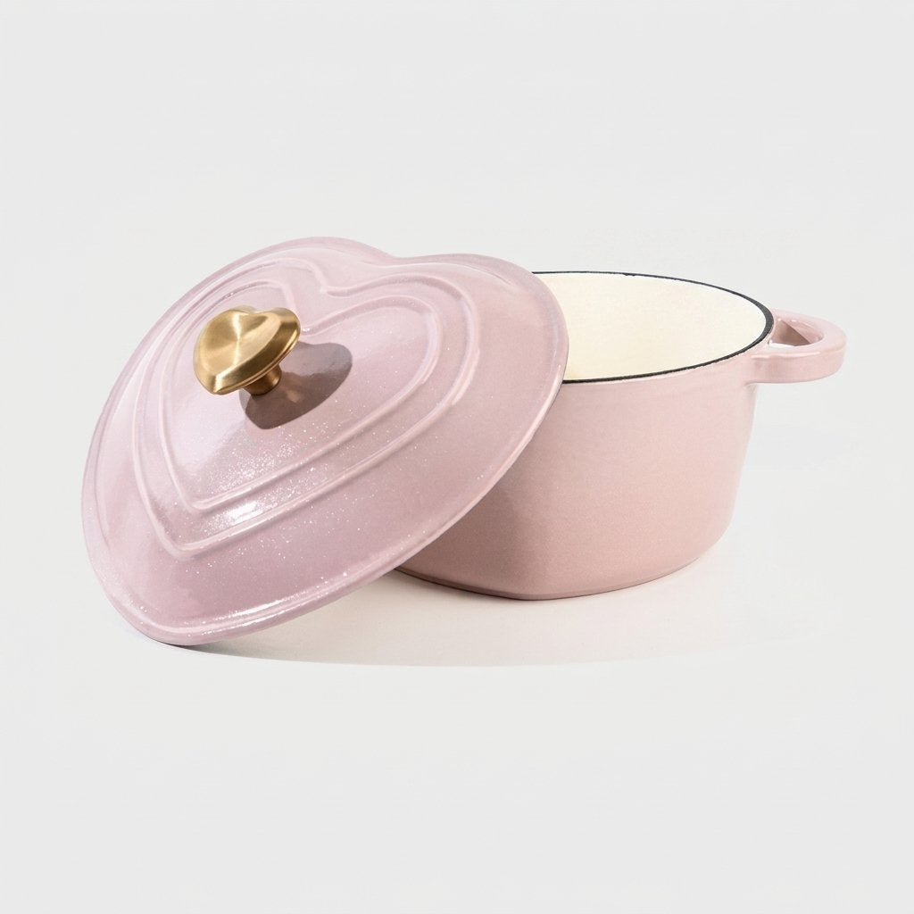 Studio product shot of the pink heart-shaped enamel pot on a plain background, lid propped against the empty pot showing the cream interior and gold heart knob