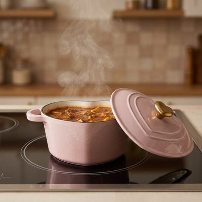 Pink heart-shaped enamel pot filled with stew on an induction stovetop, lid removed and propped against the base, steam rising