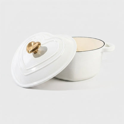Studio product shot of the white heart-shaped enamel pot on a plain background, lid propped against the empty pot showing the cream interior and gold heart knob