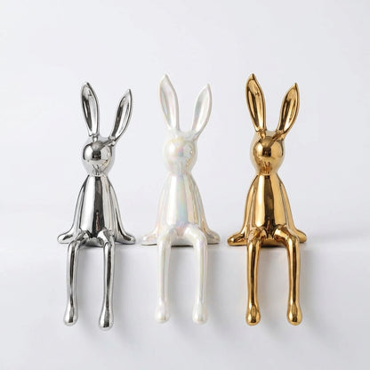 Three metallic rabbit figurines in silver, white, and gold on a light gray background