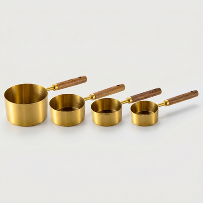 Set of four brass measuring cups with wooden handles on a light gray background