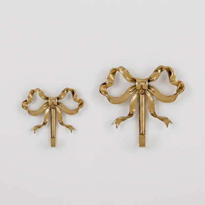 Small and large gold bow-shaped wall hooks side by side on a plain studio background