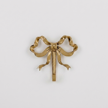Small gold bow-shaped wall hook on a plain studio background