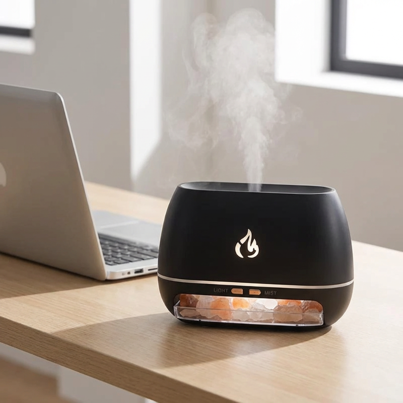 Black humidifier with flame design on a wooden desk next to a laptop.