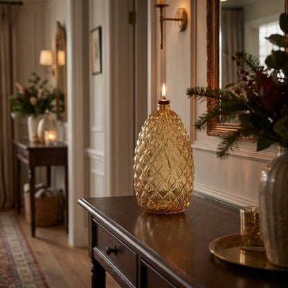 Lit Pinecone glass oil lamp on a console table in an entryway with a mirror and floral arrangement
