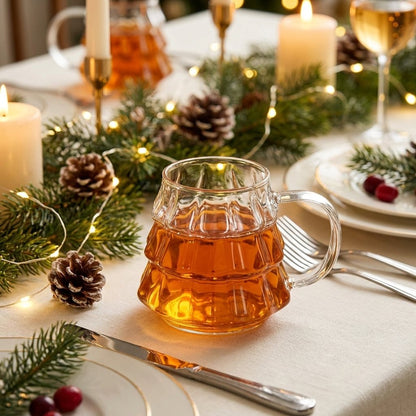 Tree-shaped glass filled with apple cider on a white linen dinner table with pinecones and candles