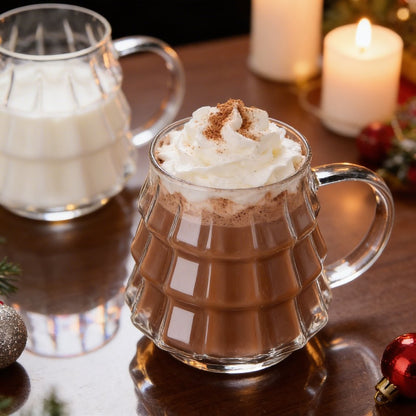 Tree-shaped glass filled with hot cocoa and whipped cream beside a second glass of milk by candlelight