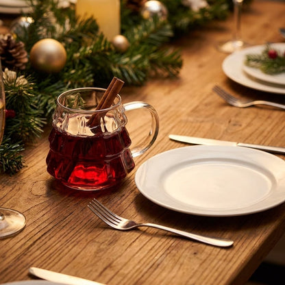 Tree-shaped glass filled with mulled wine and a cinnamon stick on a rustic table with pine greenery