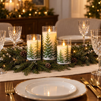 Three flameless candles printed with snowy pine trees on a dining table with an evergreen garland runner and pinecones, beside white plates, gold cutlery and crystal glasses