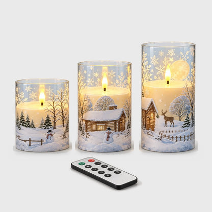 Three flameless candles of different heights with a snowy village print and a small black remote control on a plain light background
