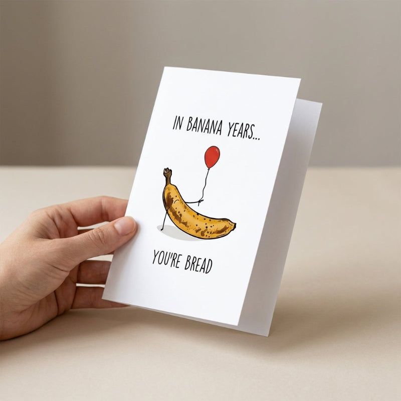 Hand holding a greeting card with a banana illustration and humorous text.