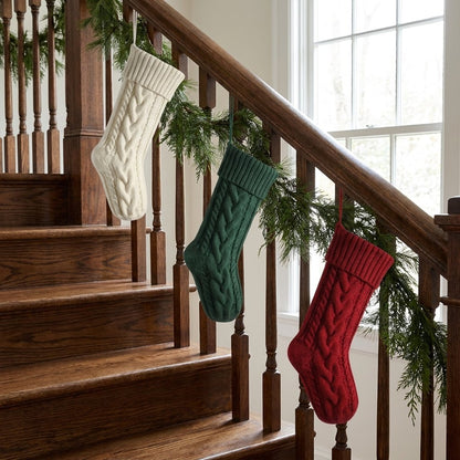 White, green, and red knit Christmas stockings hanging from a staircase banister with pine garland
