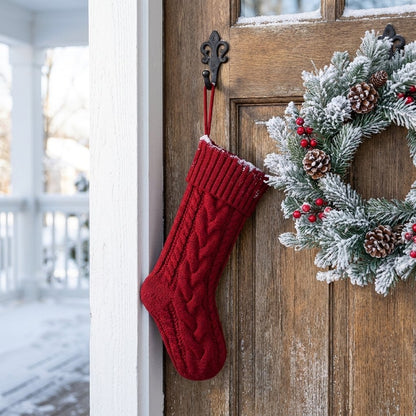 Red knit Christmas stocking hanging on a front door beside a snowy pine wreath
