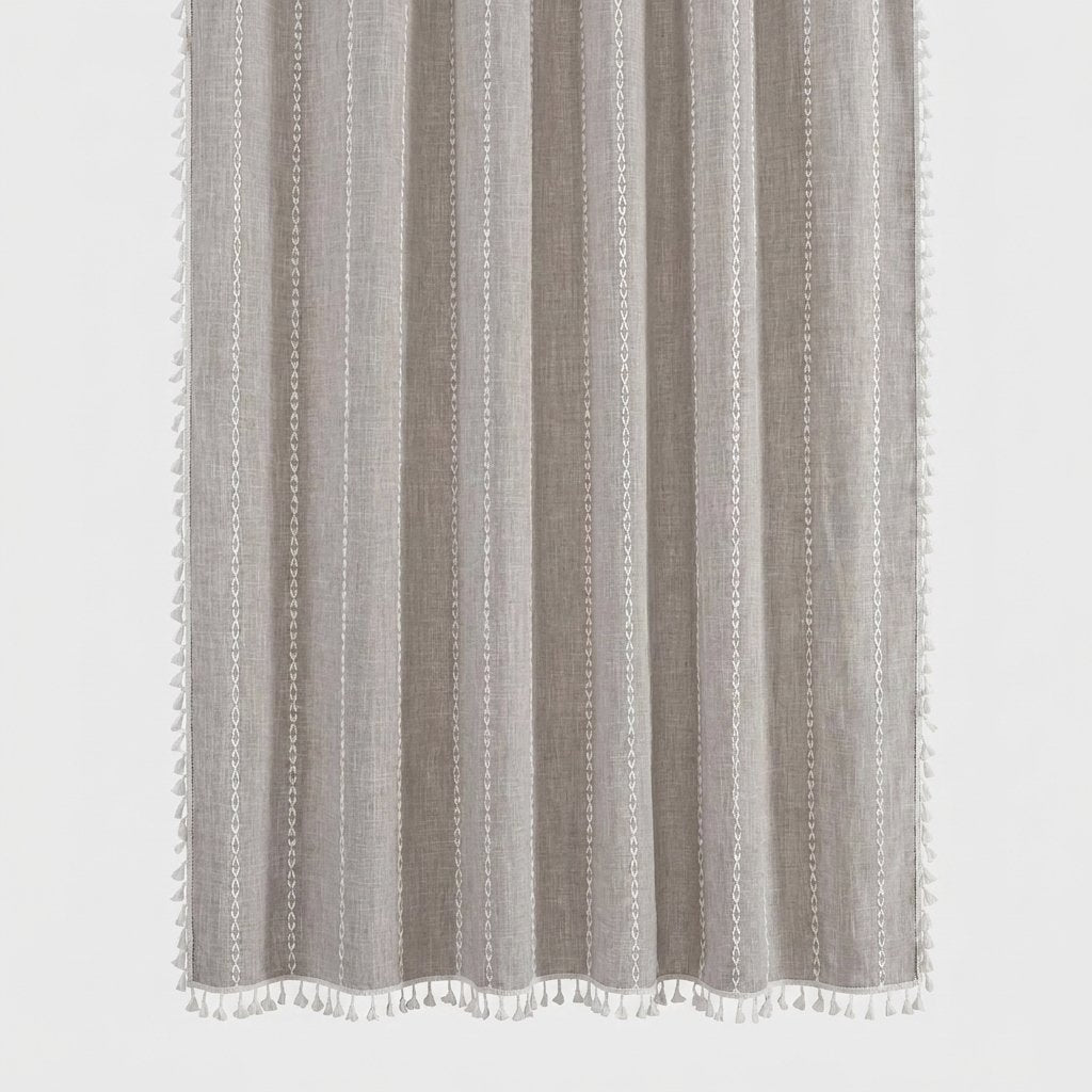 Taupe linen shower curtain with thin white stitched vertical stripes and white tassels along the hem and sides on a light grey background