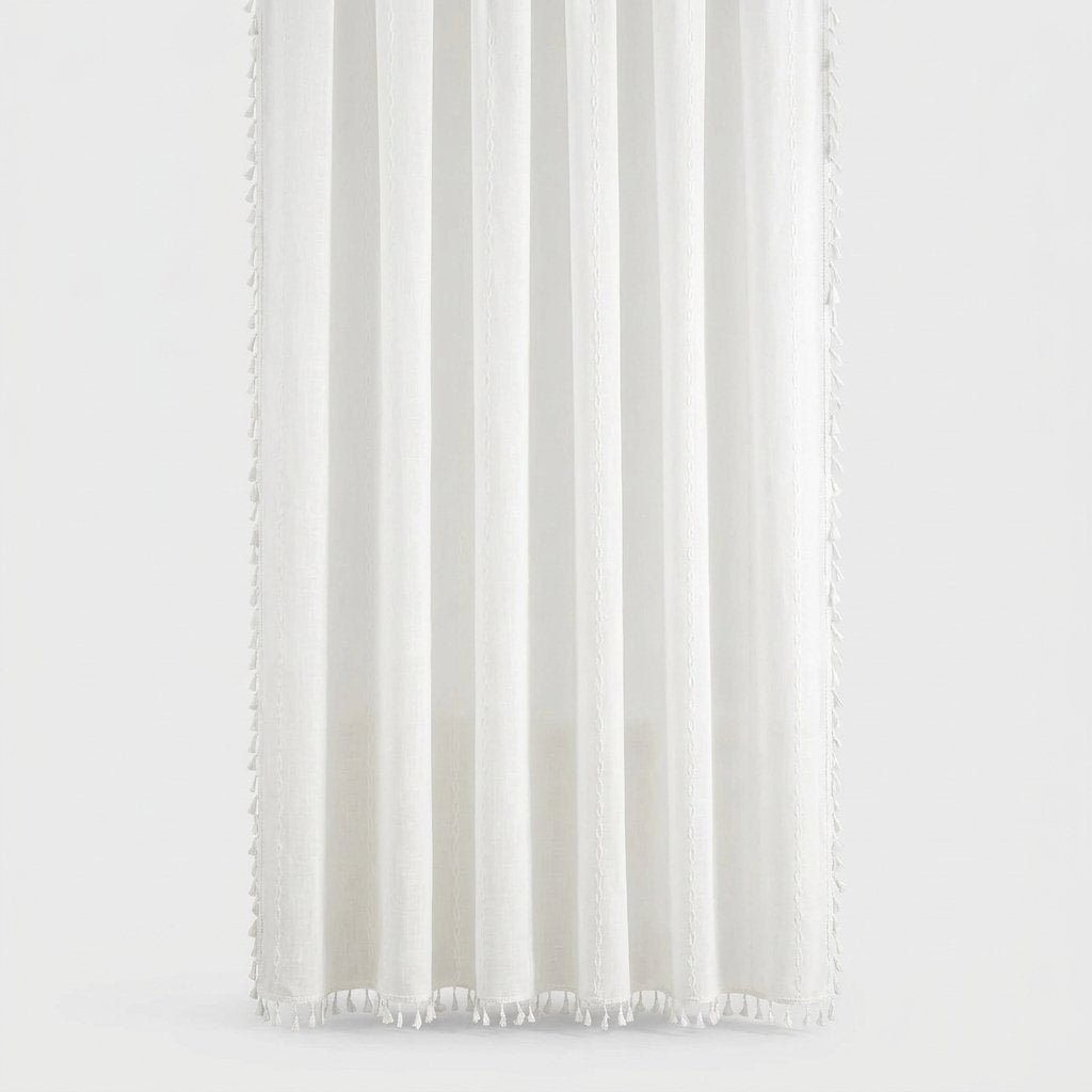 White linen shower curtain with soft vertical folds and small tassels along the hem and sides on a light grey background