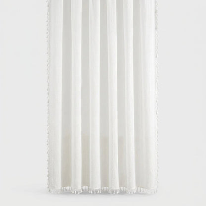 White linen shower curtain with soft vertical folds and small tassels along the hem and sides on a light grey background