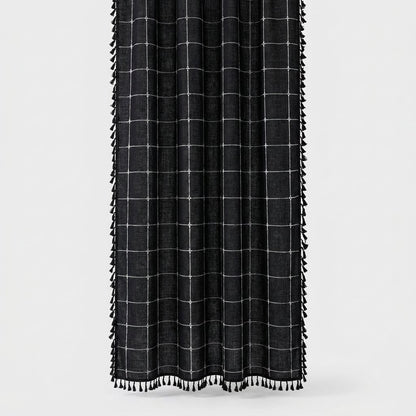 Black windowpane linen shower curtain with a thin white grid and black tassels along the sides and hem on a light background