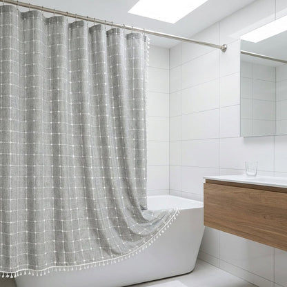 Light gray windowpane linen shower curtain with white tassels drawn open over the rim of a freestanding tub in a modern white bathroom