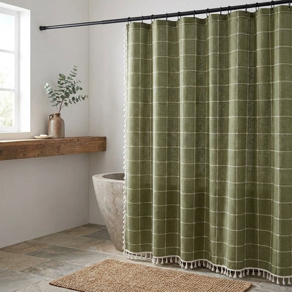 Olive green windowpane linen shower curtain with a cream grid and tassel hem beside a wood shelf with a vase of eucalyptus in a bathroom