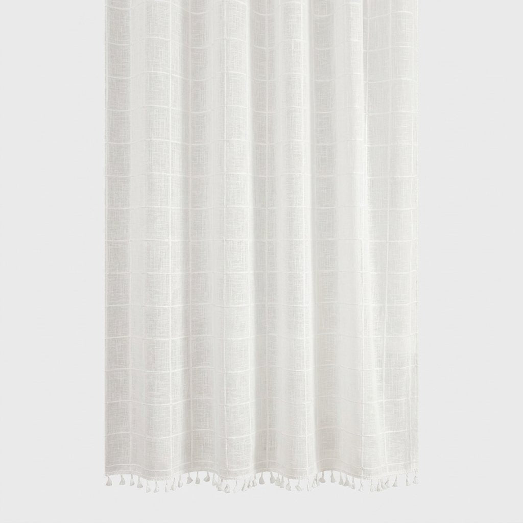 Close-up of a white semi-sheer windowpane linen shower curtain with a white tassel hem on a light grey background
