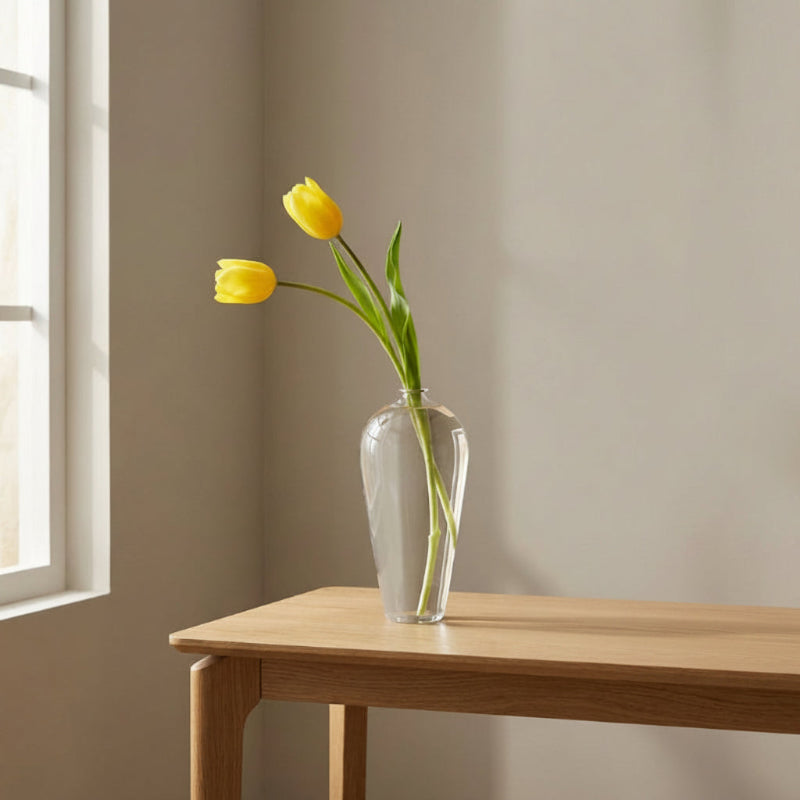 Lucia hand-blown clear glass vase with yellow tulips on side table