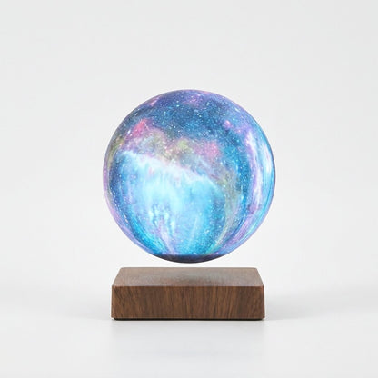 A spherical galaxy-patterned decorative object with swirling blue, purple, and pink cosmic design, displayed floating above a rectangular dark wood base on a clean white background.