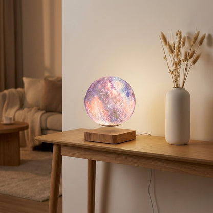 A floating moon lamp with a colorful nebula-patterned sphere on a wooden base, styled on a wooden console table next to a white vase with dried grass in a cozy living room setting.