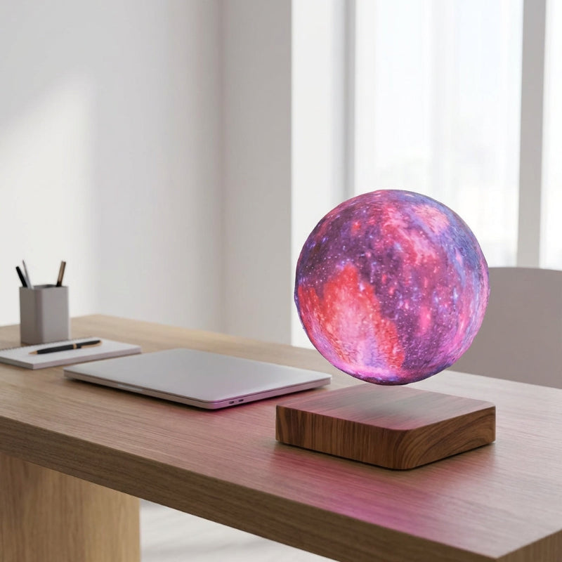 Levitating moon lamp on a desk with a laptop and stationery items.