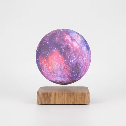 A spherical lamp or decorative orb with a purple, pink, and blue galaxy print, floating above a rectangular wooden base on a clean white background.