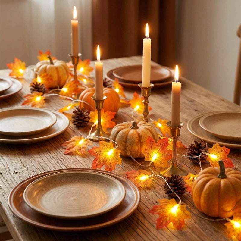 Decorative table setting with pumpkins, candles, and string lights on a wooden table.