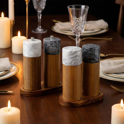 Four marble and acacia wood salt and pepper mills in white and black on two wood trays at a candlelit dinner table