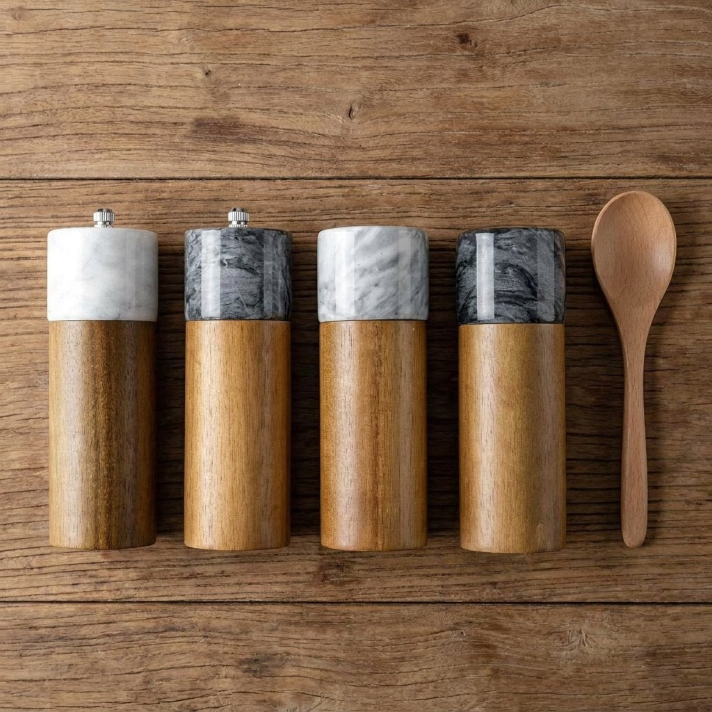 Overhead view of four white and black marble and acacia wood mills, top grinder and hidden grinder styles, beside a wooden spoon
